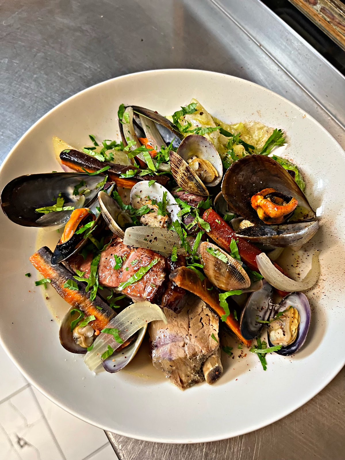 Assiette de moules et palourdes avec chorizo, légumes et herbes fraîches